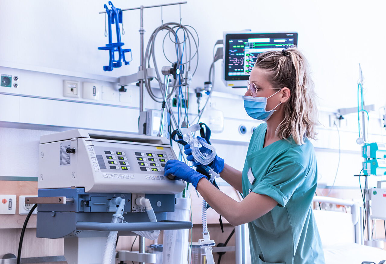 Krankenschwester mit OP-Maske trägt, überprüft die Einstellungen eines mechanischen Beatmungsgeräts mit reinem Sauestoff
